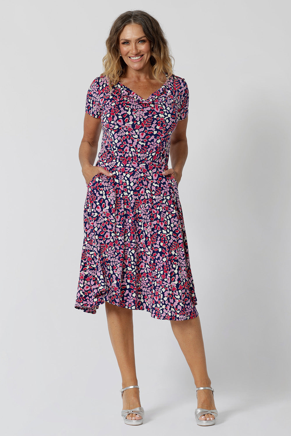 Summer dresses for over 40s women don't get much beter than this! A size 12, over 40 woman wears knee length summer dress with asymmetric hemlineand cowl neck. A short sleeve dress in pretty red, pink, white and navy print this is a good jersey dress for travel and cruise wear. Made in Australia by Australian and New Zealand women's clothes brand, Leina & Fleur, shop their petite to plus size dresses online.