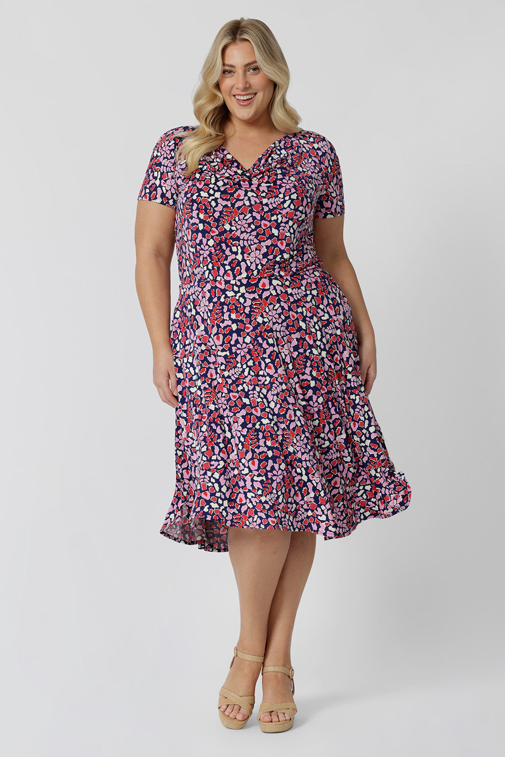 Summer dresses for curve women don't get much beter than this! A size 18, plus size woman wears knee length summer dress with asymmetric hemline and cowl neck. A short sleeve dress in pretty red, pink, white and navy print this is a good jersey dress for travel and cruise wear. Made in Australia by Australian and New Zealand women's clothes brand, Leina & Fleur, shop their petite to plus size dresses online.