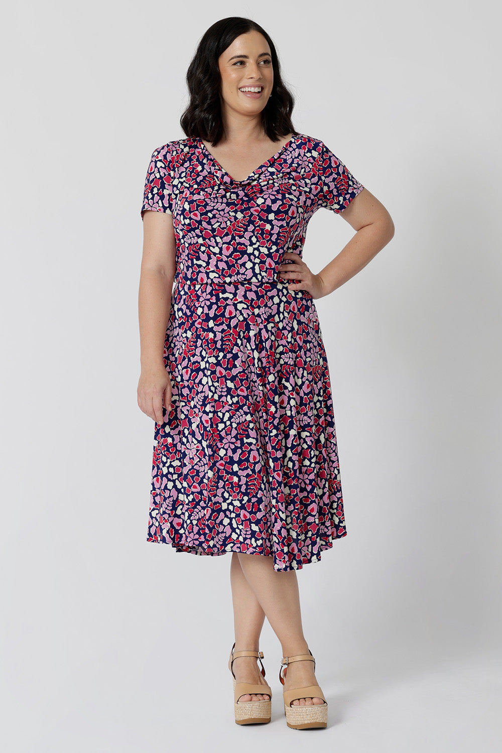 Summer dresses for petite women don't get much beter than this! A size petite size 10 woman wears knee length summer dress with asymmetric hemline and cowl neck. A short sleeve dress in pretty red, pink, white and navy print this is a good jersey dress for travel and cruise wear. Made in Australia by Australian and New Zealand women's clothes brand, Leina & Fleur, shop their petite to plus size dresses online.