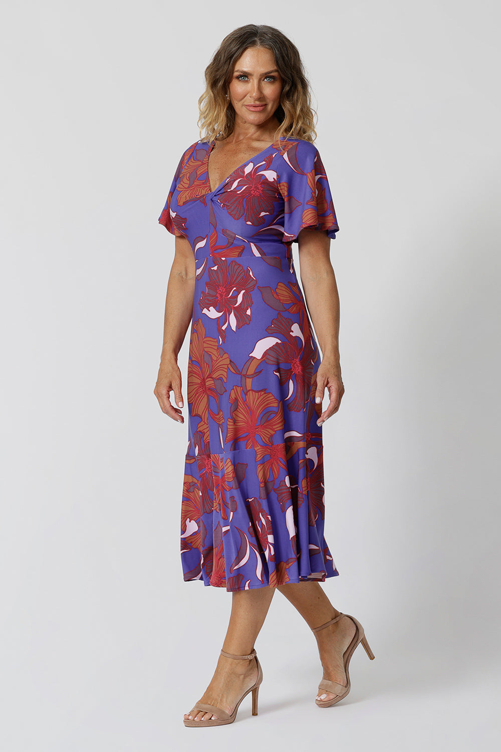 An image of a size 12, over 40 woman wears an empire line midi dress with flutter sleeves and twist front bodice. A good dress for wedding guest outfits, bold print makes it a pretty summer dress. Made in Australia by Australian and New Zealand women's clothes brand, Leina & Fleur, shop their petite to plus size dresses online.