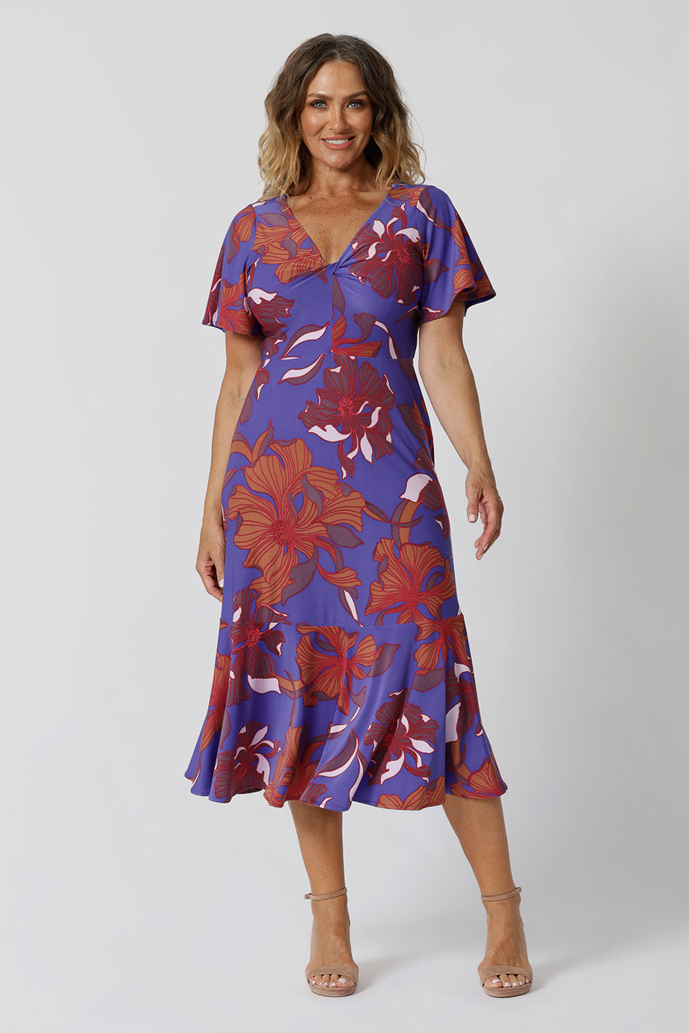 Summer dresses for over 40s women don't get much better than this! A size 12, over 40 woman wears an empire line midi dress with flutter sleeves and twist front bodice. A good dress for wedding guest outfits, bold print makes it a pretty summer dress. Made in Australia by Australian and New Zealand women's clothes brand, Leina & Fleur, shop their petite to plus size dresses online.