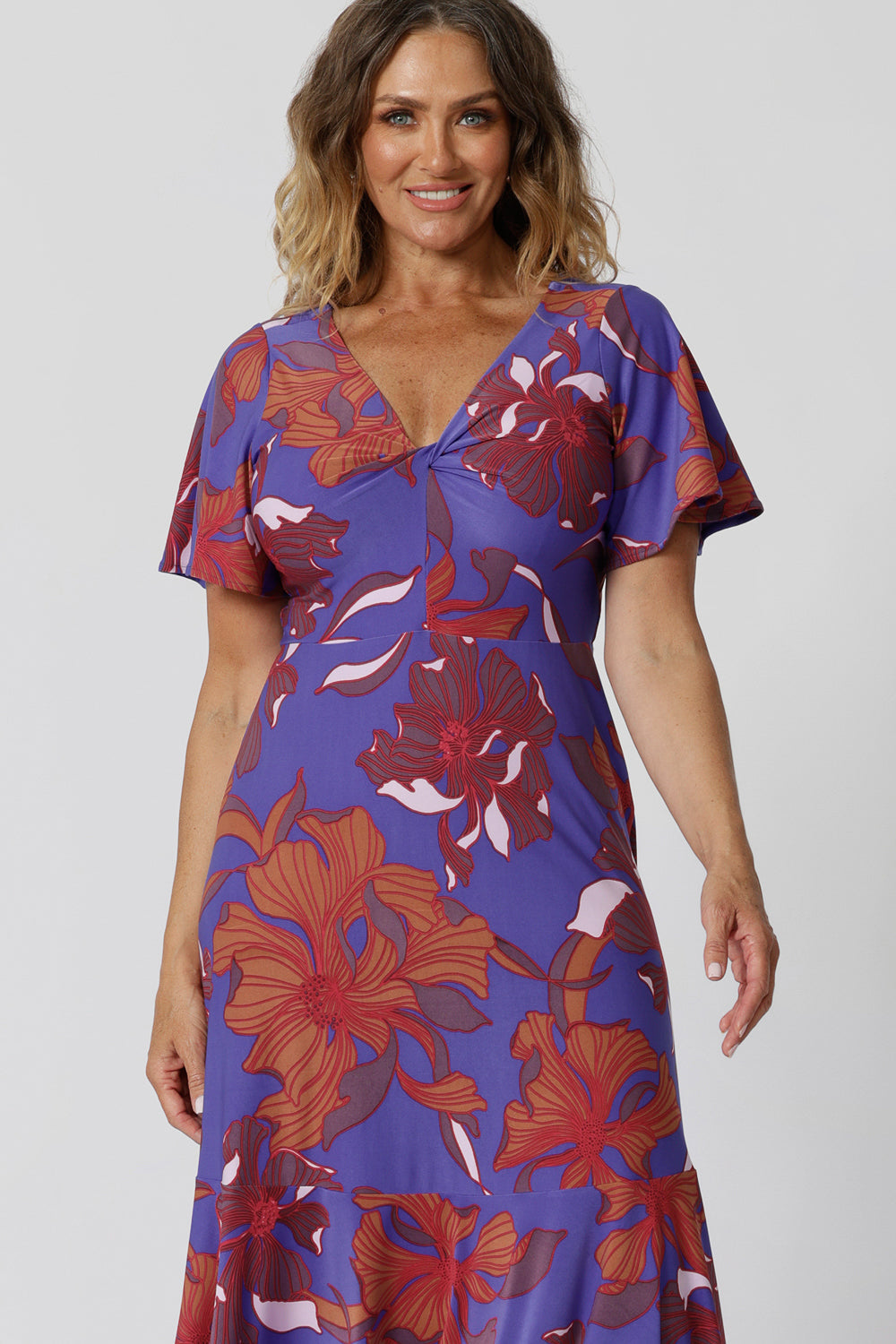 A size 12, over 40 woman wears an empire line midi dress with flutter sleeves and twist front bodice. A good dress for wedding guest outfits, bold print makes it a pretty summer dress. Made in Australia by Australian and New Zealand women's clothes brand, Leina & Fleur, shop their petite to plus size dresses online.
