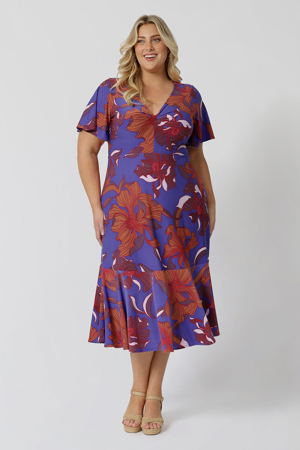 An image of a size 18 and size 20, over 30 woman wears an empire line midi dress with flutter sleeves and twist front bodice. A good dress for wedding guest outfits, bold print makes it a pretty summer dress. Made in Australia by Australian and New Zealand women's clothes brand, Leina & Fleur, shop their petite to plus size dresses online.