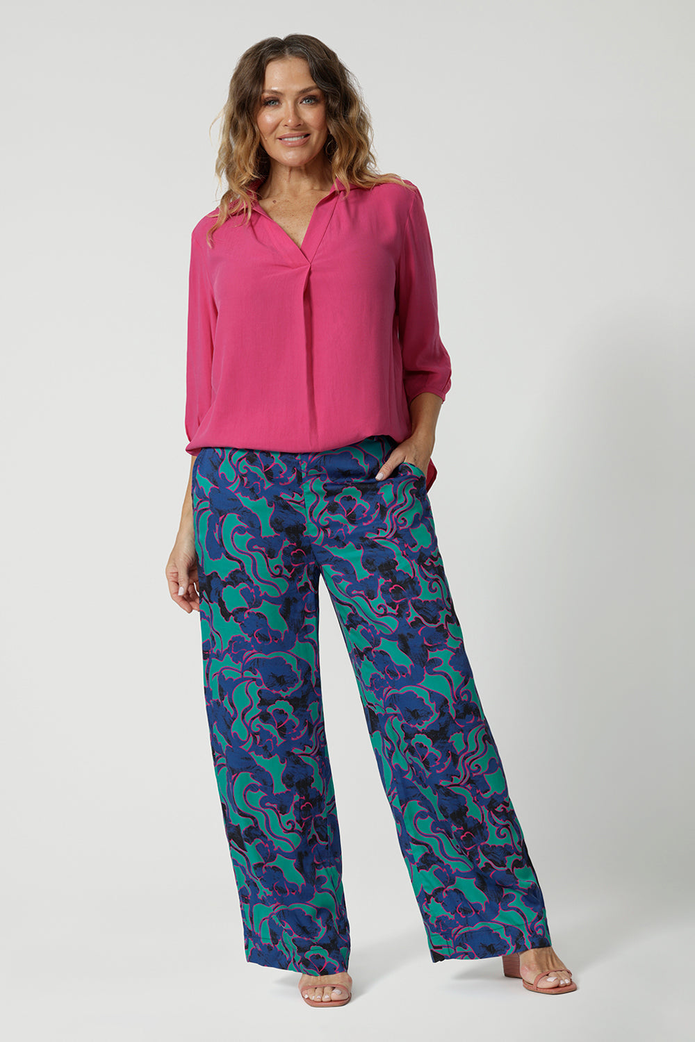 Full body front image of an over 40 woman, wearing long wide pants with an abstract pattern. Made of easy to care satin rayon fabric displaying aqua blue, navy and pink colours. This Australian made product was made by woman in Australia and New Zealand. Leina & Fleur is a woman’s online clothing brand that has sizes ranging from 8 to 24 including plus sizes and petite sizes.