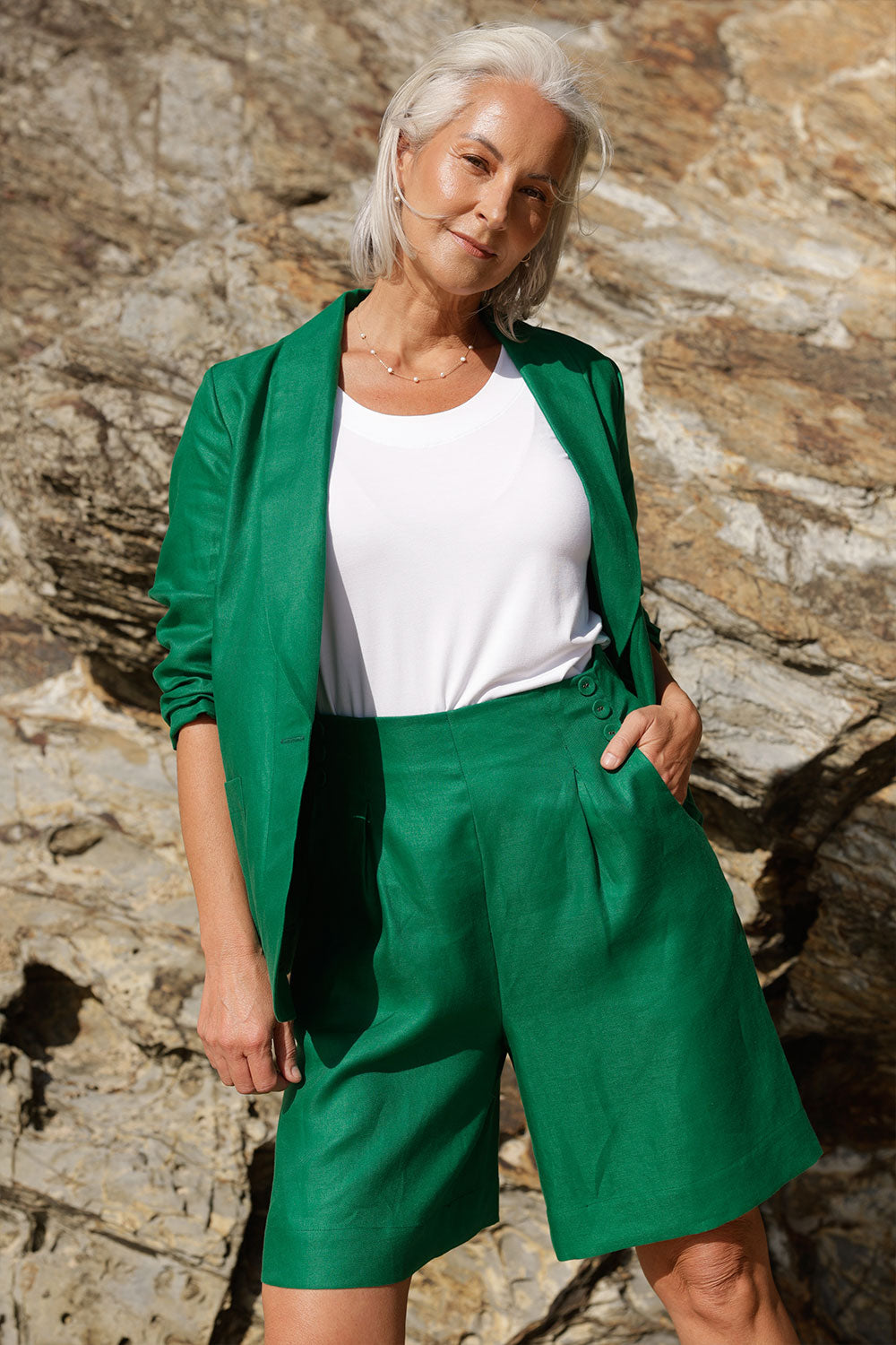 A mature woman wears 100% Linen Bermuda shorts. The perfect smart casual shorts suitable for summer workwear to take you through to the weekend. Styled back with a soft tailored emerald green linen blazer. Both in a beautiful emerald green colour and soft tailoring details. Designed and made in Australia for sizes 8 -24.