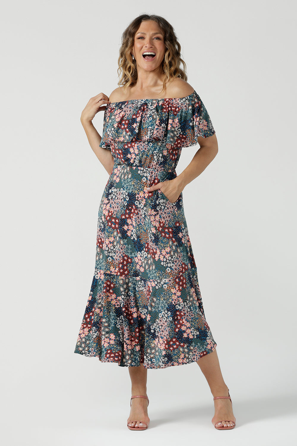 A woman wears the Myla dress in Whimsy an off shoulder frill neck style. Side pockets and frill hem. Made in Australia and size inclusive for women size 8-24.