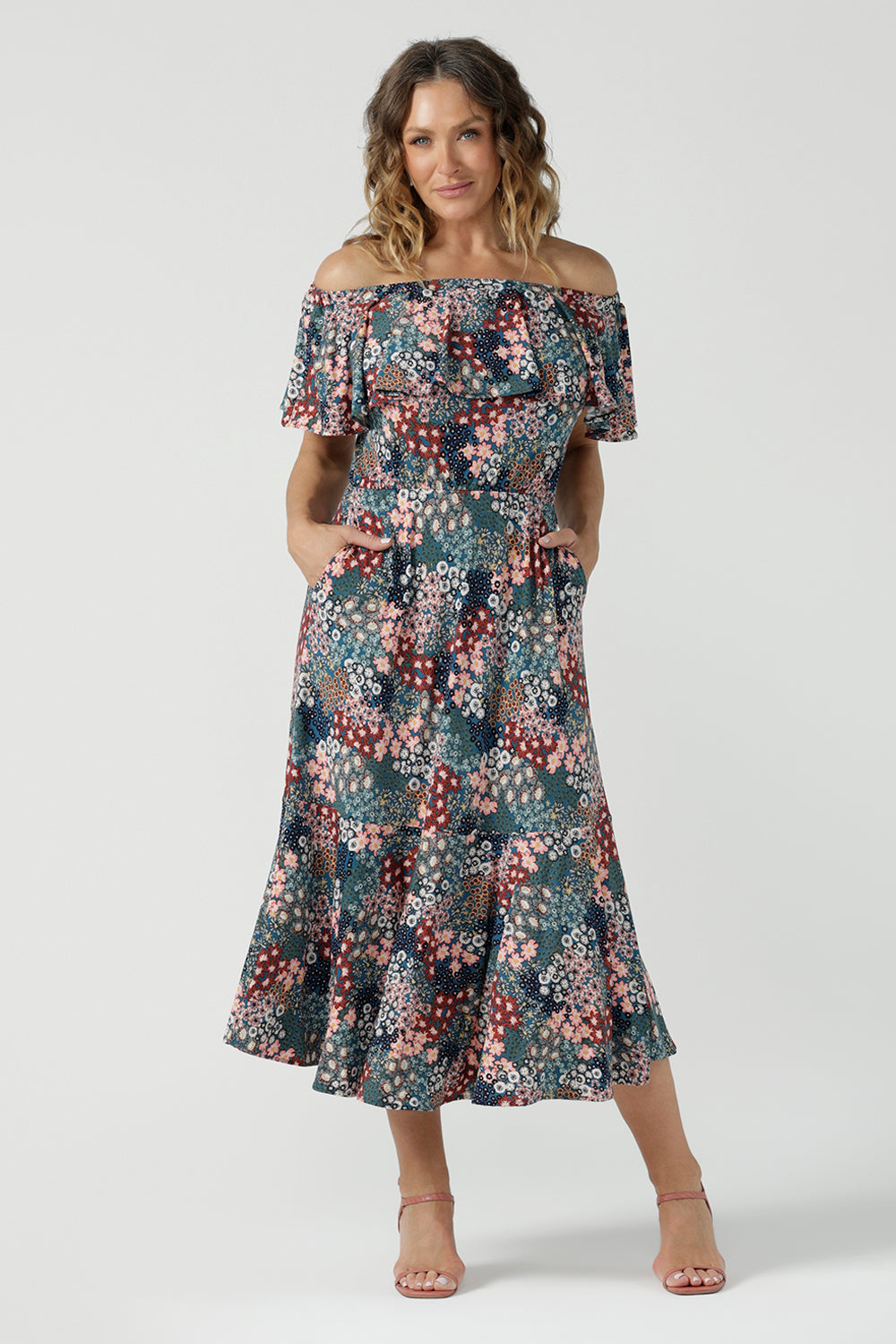 Worn on one shoulder. A woman wears the Myla dress in Whimsy an off shoulder frill neck style. Side pockets and frill hem. Made in Australia and size inclusive for women size 8-24.