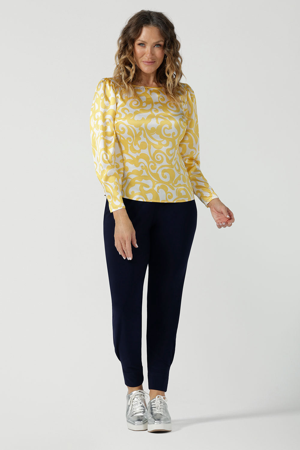 A size 10 woman wears a Zara Top in Yellow Swirl silk. A long sleeve blouse with fashion sleeve and made in 100% silk. Made in Australia for women size 8-24. Styled back with the Indi Tall Pant in Navy.