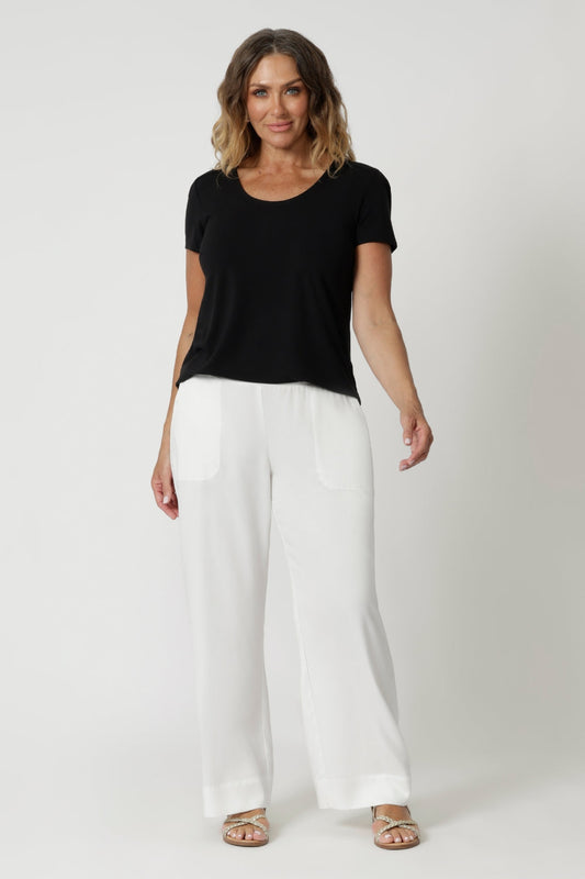 Over 40's woman wears short sleeved black top made from bamboo fabric, perfect for style and comfort. Travel ready top features a shirttail hemline & scoop neckline. Leina & Fleur stock this top in sizes 8-24 keeping in mind petite & plus sizes.