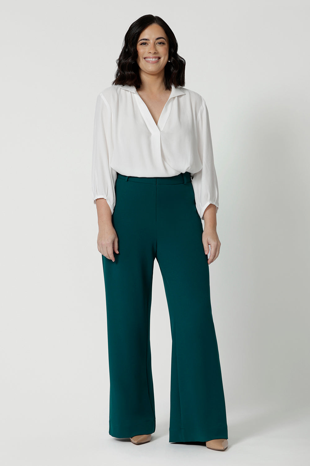 Showing good workwear pants for petite women,  Green scuba crepe wide leg pants are worn with a white work shirt. These wide leg work trousers are made in Australia by Australia and New Zealand women's clothes brand, Leina & Fleur. Available to shop in sizes 8 to 24, this is workwear for plus size to petite height women. 