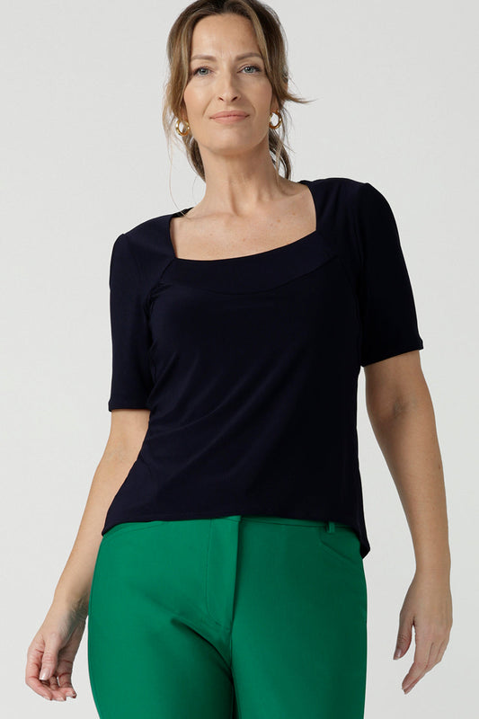 A size 10 over 40 year old woman wears a casual jersey top in navy blue, styled with emerald green pants. This Australian-made women's top has short fitted sleeves, a square neckline and and high-low - perfect for weekend casual and travel capsule wardrobes.