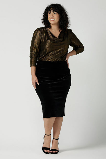 Woman wears the Brooke Skirt in Black Velour. Slim fit tube skirt for evening wear. Flattering style. Size inclusive fashion Australian made size 8 - 24. Styled back with black high heel and cowl neck gold Chrissy Top.