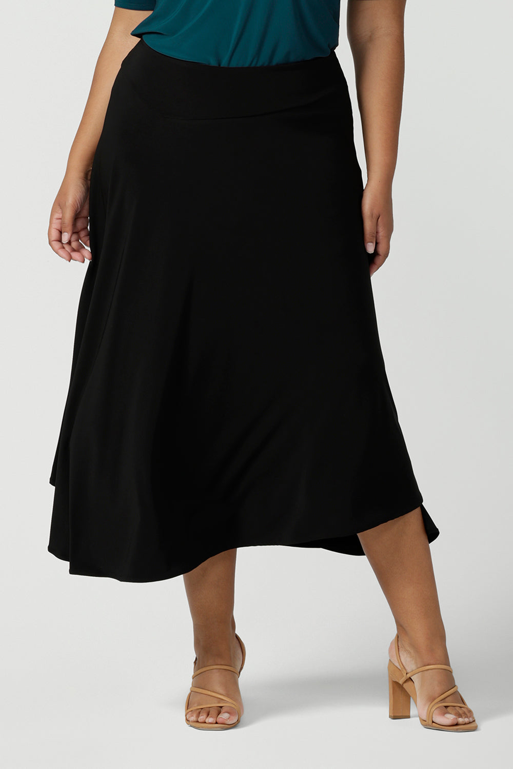Close up of a size 18, plus size woman wears an asymmetric skirt in black jersey. Worn with a teal green short sleeve top with square neck, this comfortable jersey skirt works for work wear and eveningwear. Made in Australia by women's clothing brand, Leina & Fleur in petite, mid size and plus sizes. 