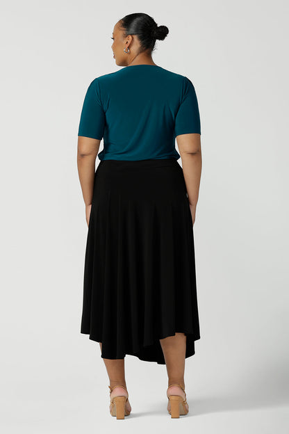 Back view of a size 18, plus size woman wears an asymmetric skirt in black jersey. Worn with a teal green short sleeve top with square neck, this comfortable jersey skirt works for work wear and eveningwear. Made in Australia by women's clothing brand, Leina & Fleur in petite, mid size and plus sizes. 