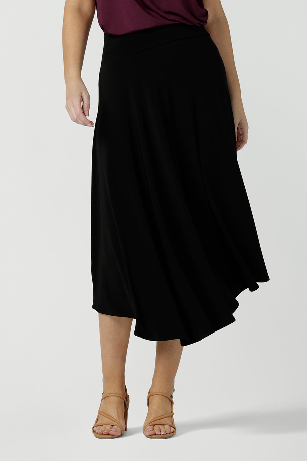 A size 10, 40 plus woman wears an asymmetric skirt in black jersey.  An easy-care skirt, this comfortable, knee-length jersey skirt works for work wear and eveningwear. Made in Australia by women's clothing brand, Leina & Fleur in petite, mid size and plus sizes. 