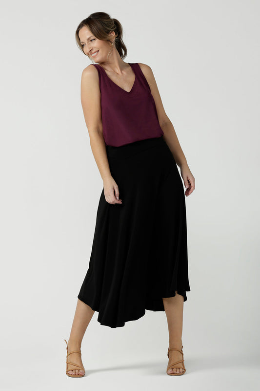 A size 10, 40 plus woman wears an asymmetric skirt in black jersey. Worn with a plum red cami top, this comfortable jersey skirt works for work wear and eveningwear. Made in Australia by women's clothing brand, Leina & Fleur in petite, mid size and plus sizes. 