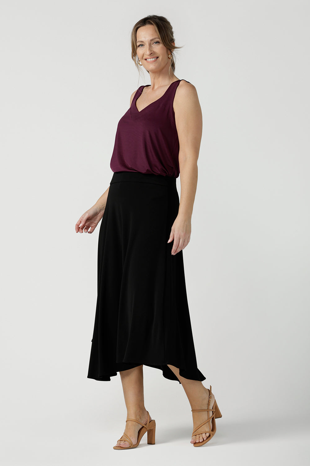A size 10  woman wears an asymmetric skirt in black jersey. Worn with a plum red cami top, this comfortable jersey skirt works for work wear, casual wear and eveningwear. Made in Australia by women's clothing brand, Leina & Fleur in petite, mid size and plus sizes. 
