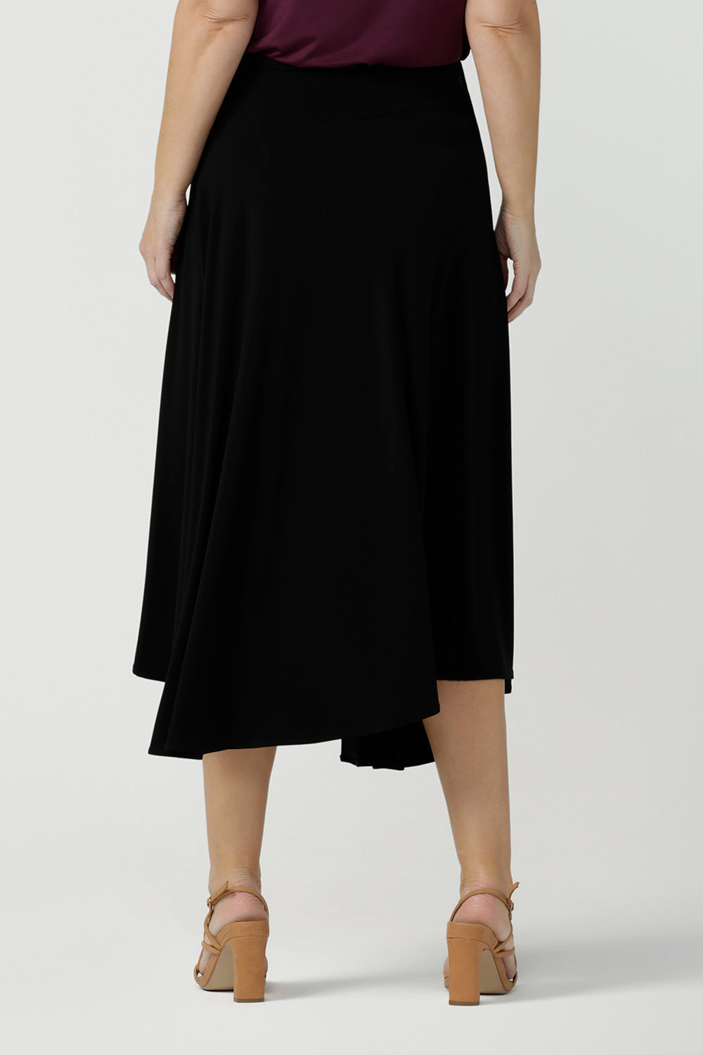 Back view of a size 10, 40 plus woman wears an asymmetric skirt in black jersey. Worn with a plum red cami top, this comfortable jersey skirt works for work wear and eveningwear. Made in Australia by women's clothing brand, Leina & Fleur in petite, mid size and plus sizes. 