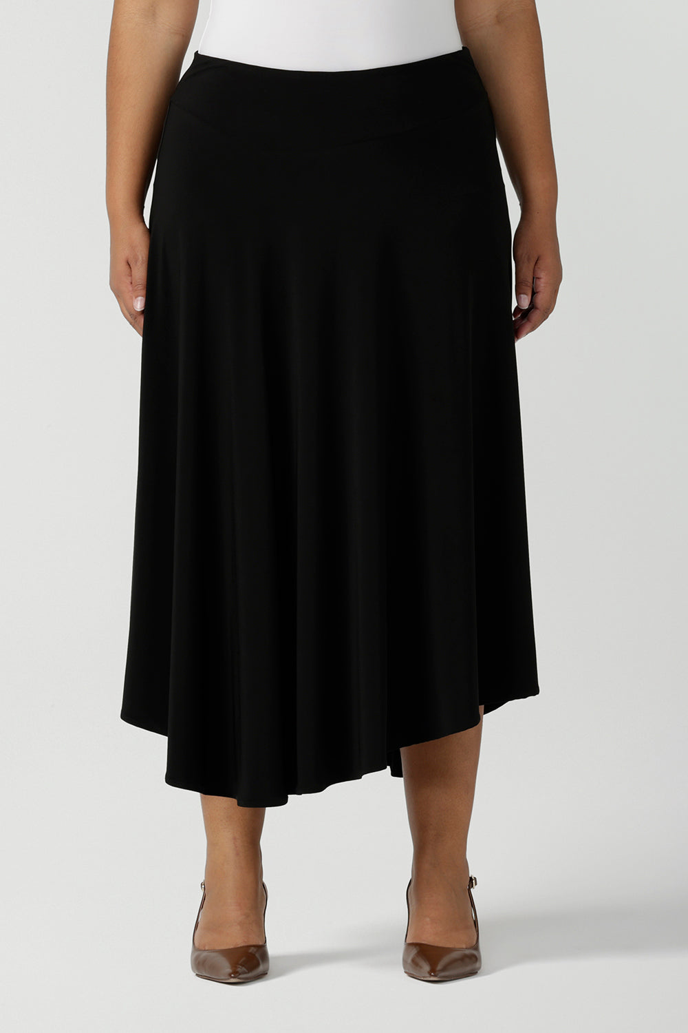 A size 18, plus size woman wears an asymmetric skirt in black jersey. This easy-care, comfortable jersey skirt works for work wear and eveningwear. Made in Australia by women's clothing brand, Leina & Fleur in petite, mid size and plus sizes. 