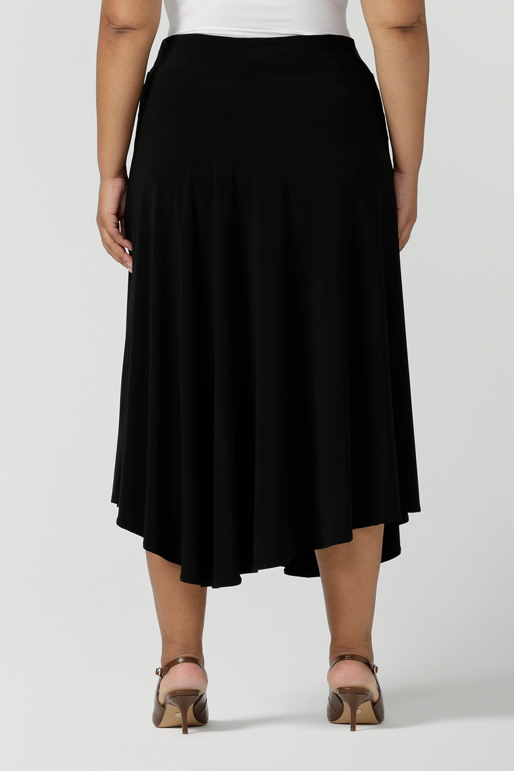 Back view of a size 18, plus size woman wears an asymmetric skirt in black jersey. This easy-care, comfortable jersey skirt works for work wear and eveningwear. Made in Australia by women's clothing brand, Leina & Fleur in petite, mid size and plus sizes.