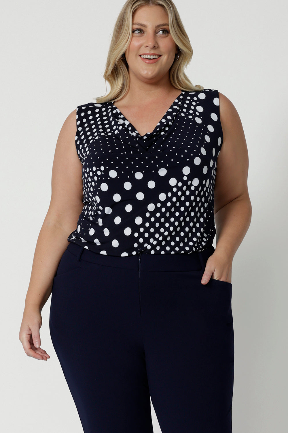 Showing a summer top for curvy women, a size 18, plus size women wears a cowl neck jersey top. This sleeveless top has a navy and white spot print - great for corporate wear as well as casual wear! Made in Australia by Australian and New Zealand clothing brand, Leina & Fleur, shop this top in petite to plus sizes. 