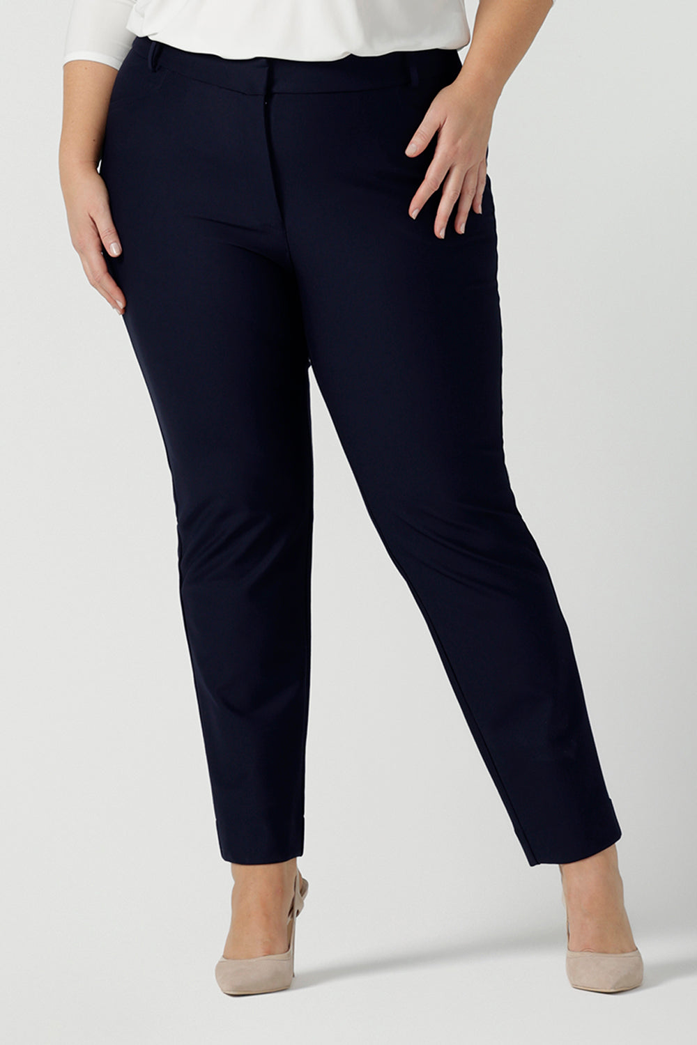 Close up of a a size 18 woman wears the Lulu tailored pant in Navy. Made in Australia for women. A tailored pant in Navy with waistband and fly front with pockets. Styled back with the Jules. Size inclusive 8 - 24.