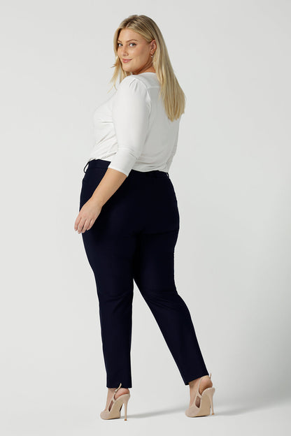 A size 18 woman wears the Lulu tailored pant in Navy. Made in Australia for women. A tailored pant in Navy with waistband and fly front with pockets. Styled back with the Jules. Size inclusive 8 - 24.