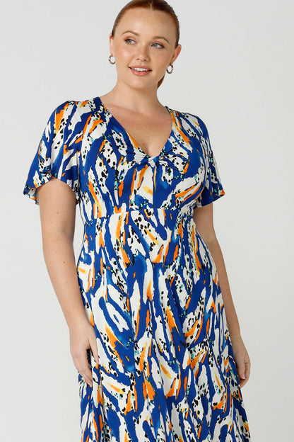 Close up detailed view of a curvy size, size 12 woman wearing a casual slinky jersey midi dress in an abstract print. The dress has short flutter sleeves, a double layer twist front bodice and an asymmetrical skirt - this is a great dress for weekend and travel style.