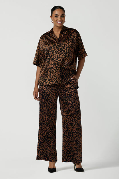 A woman wears the Sloane Pant in Bronze Animal. A satin straight leg waisted pant with pockets and a zip front. Made in high fashion Animal print fabric. Petite to plus size women size 8-24. Styled back with the Pele Shirt in Bronze animal.