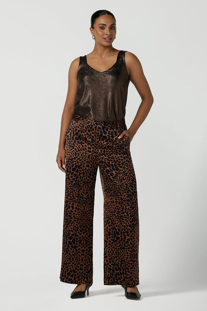 A woman wears the Sloane Pant in Bronze Animal. A satin straight leg waisted pant with pockets and a zip front. Made in high fashion Animal print fabric. Petite to plus size women size 8-24. 