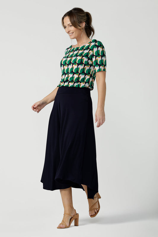 A size 10, 40 plus woman wears an asymmetric skirt in navy jersey. Worn with a geometric print, boat neck top with short sleeves, this comfortable jersey skirt works for work wear and eveningwear. Made in Australia by women's clothing brand, Leina & Fleur in petite, mid size and plus sizes.