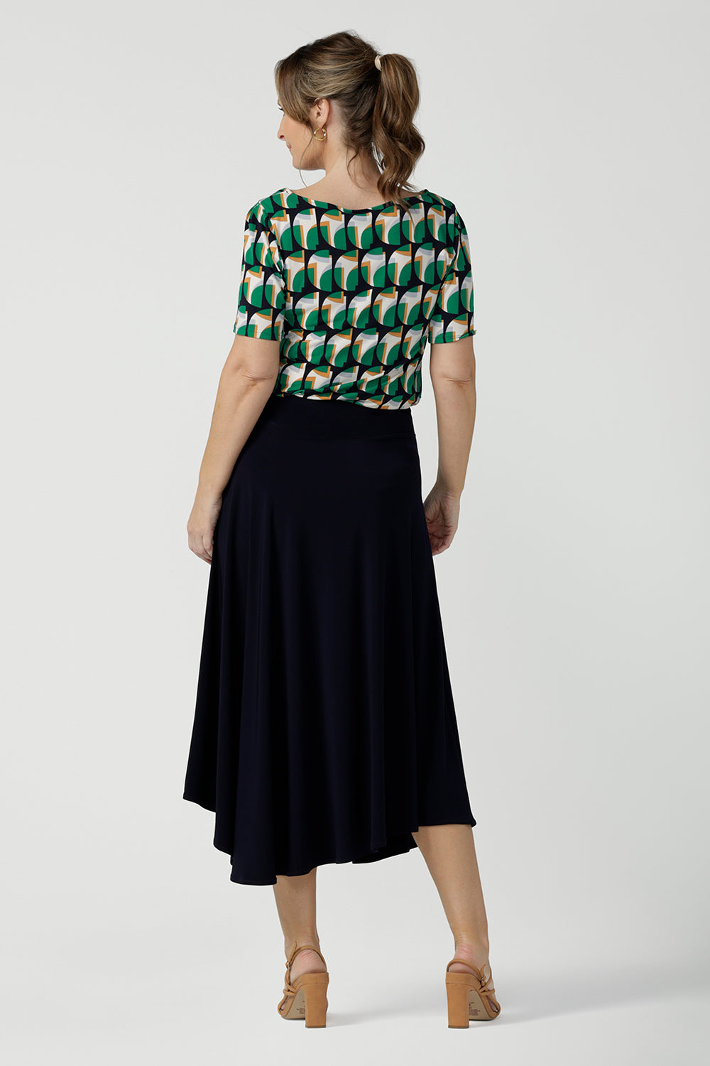 Back view of a size 10, 40 plus woman wears an asymmetric skirt in navy jersey. Worn with a geometric print, boat neck top with short sleeves, this comfortable jersey skirt works for work wear and eveningwear. Made in Australia by women's clothing brand, Leina & Fleur in petite, mid size and plus sizes.
