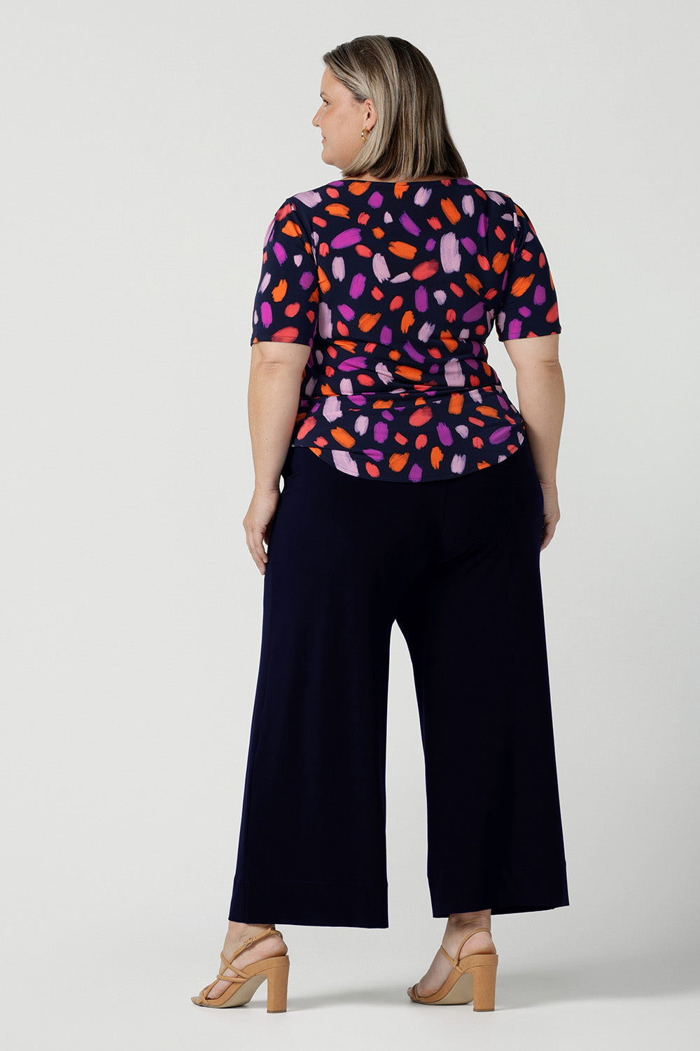 Size 18 curvy woman wears the Ziggy top in Palette. A boat neckline style with short sleeves and shoulder tucks. A great work to weekend top for women. Palette print features a brush stroke print of fuchsia, lilac, red and orange . Made in Australia for women size 8 to 24.Styled back with Bradley culottes in Navy.