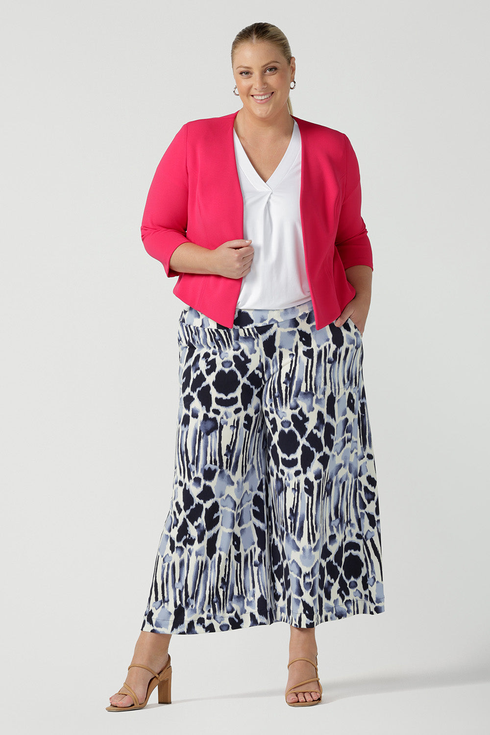 A size 18, plus size woman wears cropped, wide leg culotte pants in blue and white print with a short sleeve, white top in bamboo jersey and a work jacket in watermelon pink. Styled as summer work pants, these culottes are easy care and comfortable for office wear  as well as casual wear. Made in Australia by Australian women's clothing brand, Leina & Fleur