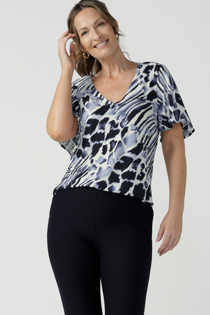 A size 10, 40 plus woman wears a blue and white print jersey, V-neck top with flutter sleeves. A good top for summer casual wear or as a short sleeve work wear top, this Australian-made top is easy to wear and easy care. Shop made in Australia tops in petite to plus sizes online at Australian women's clothing brand, Leina & Fleur.