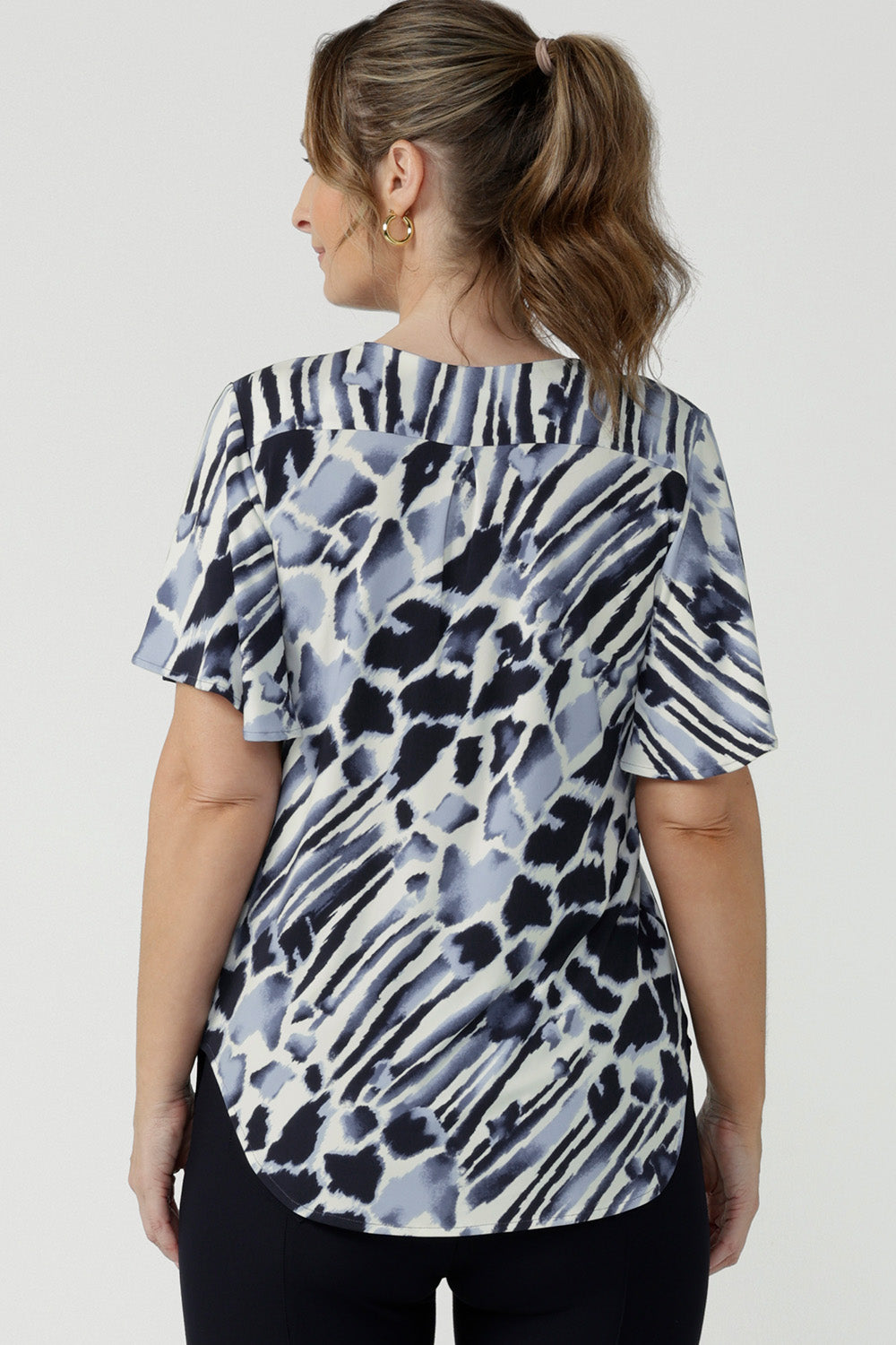 Back view of a size 10, 40 plus woman wearing a blue and white print jersey, V-neck top with flutter sleeves. A good top for summer casual wear or as a workwear top, this Australian-made top is easy to wear and easy care. Shop made in Australia tops in petite to plus sizes online at Australian fashion brand, Leina & Fleur.