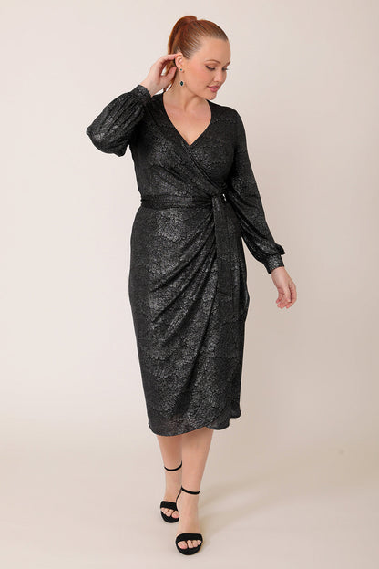 A woman wears a good cocktail dress for curvy women. A long sleeve wrap dress, this event dress shimmer in metallic foil print. A statement evening dress, wedding guest outfit or going out dress, the Carys dress is made in Australia by occasionwear brand Leina & Fleur.