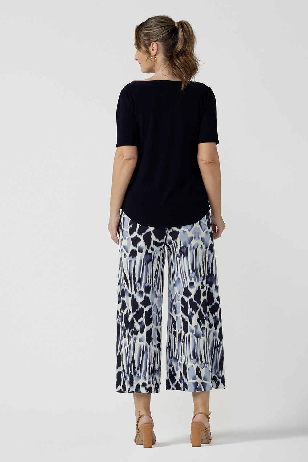 Back view of a size 10, 40 plus woman wearing cropped, wide leg culotte pants in blue and white print with a short sleeve, boat neck navy blue top. Great summer pants, these culottes are easy care trousers and are comfortable as work wear pants or for casual wear. Made in Australia by Australian women's clothes brand, Leina & Fleur.