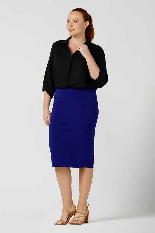 Good work wear for plus size women, a knee-length tube skirt in cobalt blue is worn with a 3/4 sleeve shirt in black. The model is a size 12 fuller figure woman. Made in Australia, shop this work skirt online in sizes 8 to 24.