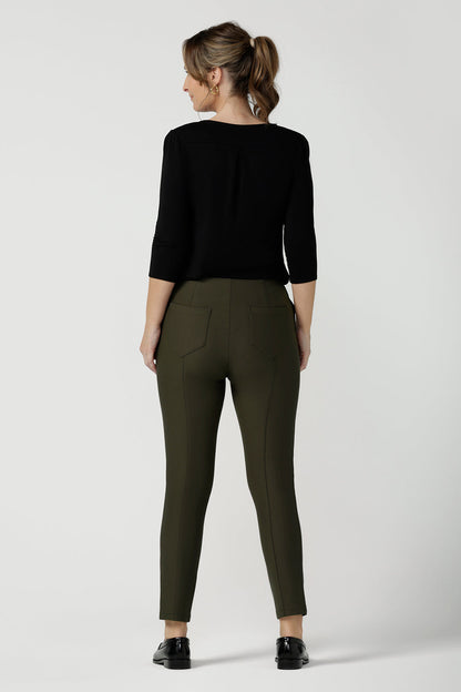 Back view of a size 10, 40 plus woman wearing slim leg, cropped length pants in olive green with a 3/4 sleeve black top.  Tailored skinny pants with pockets and a front zip fastening these made-in-Australia  work pants fit petite, mid size and plus size women.