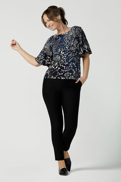 A size 10 over 40 year old woman wears a jersey top in animal print on a navy base, styled with black, fitted pants. This Australian-made women's top has flutter sleeves, a high, round neckline and and high-low hem perfect for weekend casual and travel capsule wardrobes.