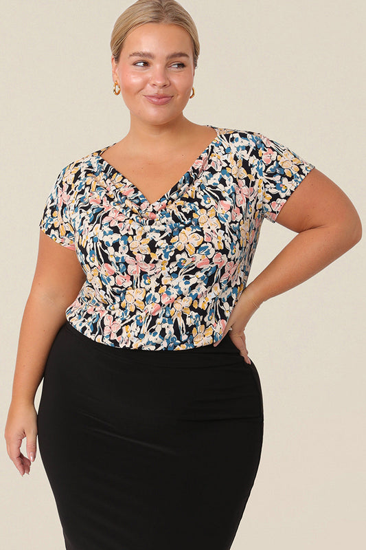A plus size, size 14 woman wears a casual jersey top. The top has short sleeves, a cowl neckline and is printed with a floral pattern for a casual weekend look.