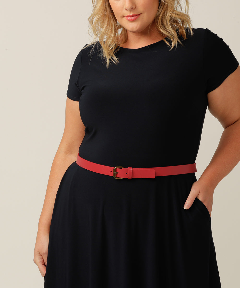 A black dress is adorned with a petite red leatherette belt featuring a silver buckle, worn by a plus-size model around her waist.