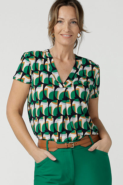 A size 10 woman wears a v-neck short sleeve jersey top in a geometric print. She wears the top. Designed and made in Australia for petite to plus size women.