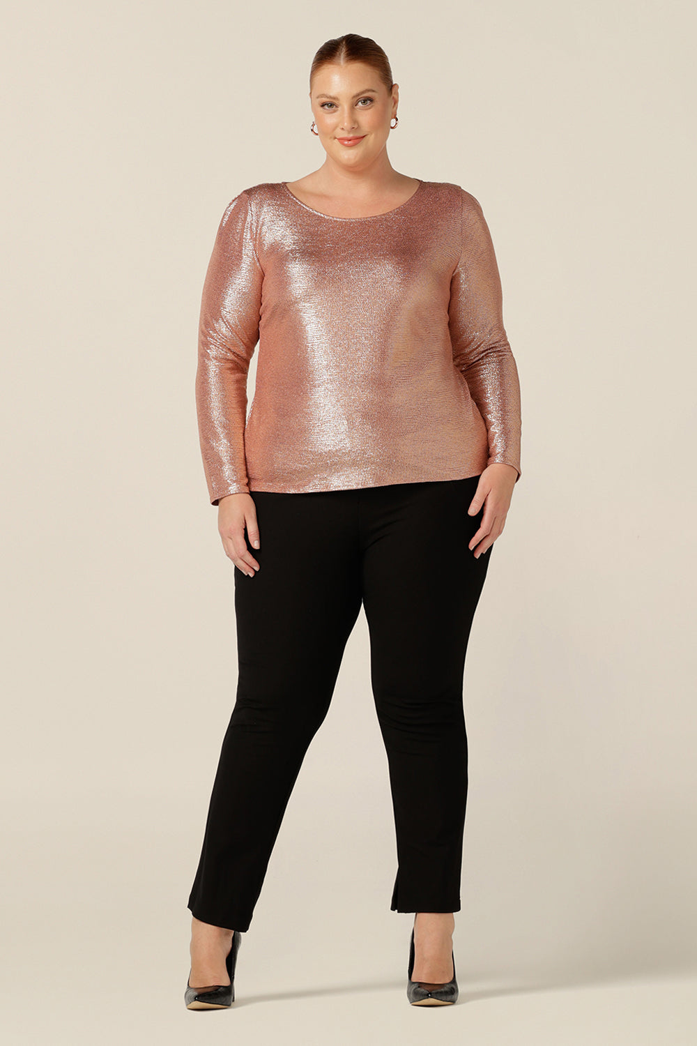 A fuller figure, size 18 woman wears a sparkly top  in shimmering pink jersey top. With a high scoop neck and long sleeves, this a modest eveningwear top that's great for plus size and 40 plus fashionable women. 