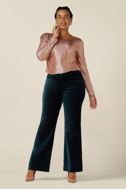 A size 12 woman wears a shimmering pink sparkly top with high scoop neck and long sleeves, with flared leg, evening trousers in petrol green velveteen. Simple and easy-to-wear, this comfortable special occasion top is made in Australia in sizes 8 to 24. 
