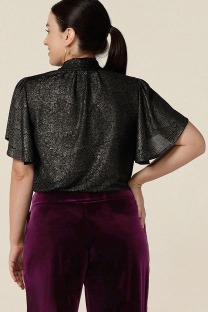 Back view of a petite height woman wearing a good top for women's evening and event wear. In shimmering bronze foil print, this V-neck top with short flutter sleeves is made in Australia by women's occasionwear brand, Leina and Fleur.