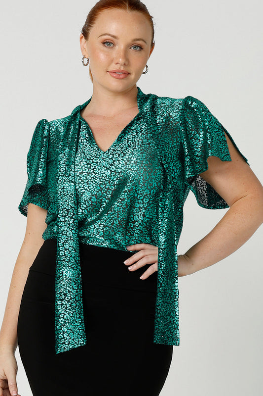 A size, size 12 woman wears a good top for curvy women's evening and event wear. In shimmering jade metallic print, this V-neck top with short flutter sleeves is made in Australia by women's fashion brand, Leina and Fleur