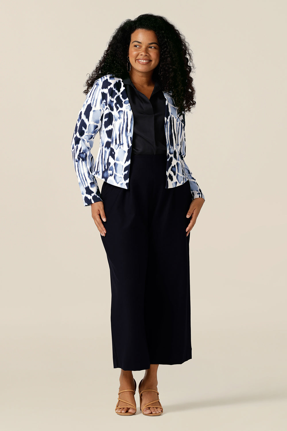  A size 12, curvy woman wears a collarless open front jacket for work and corporate wear. In navy and white jersey, this is a tailored jacket with stretch for all-day wear as a comfortable office jacket. Styled with a navy blue shirt and navy pants, this women's corporate jacket completes the work wear outfit.