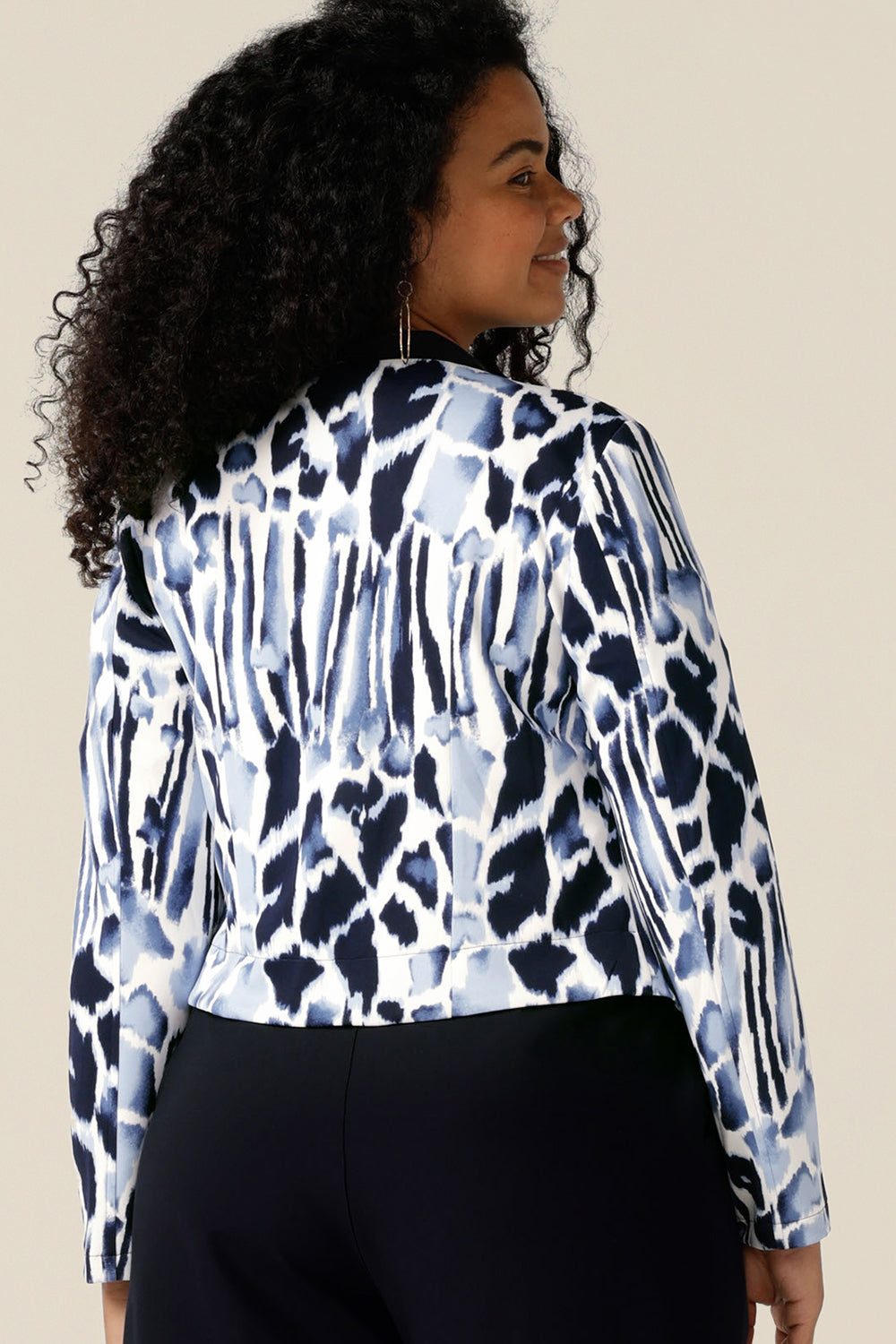A size 12, curvy woman wears a collarless open front jacket for work and corporate wear. In navy and white jersey, this is a tailored jacket with stretch for all-day wear as a comfortable office jacket. Made in Australia and shipping to New Zealand, buy this quality work jacket in sizes 8 to size 24.